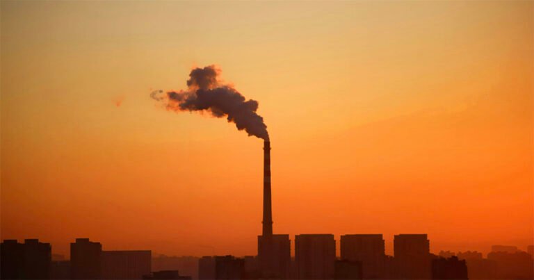 gases poluentes emitidos de planta industrial vista de cima, com céu alaranjado ao fundo