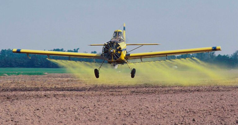 avião pulverizando substâncias químicas, com fumaça amarela, em um campo agrícola.