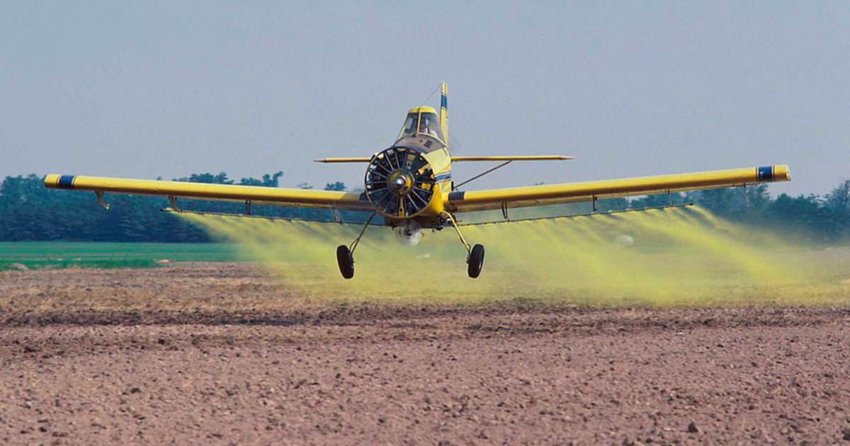 avião pulverizando substâncias químicas, com fumaça amarela, em um campo agrícola.