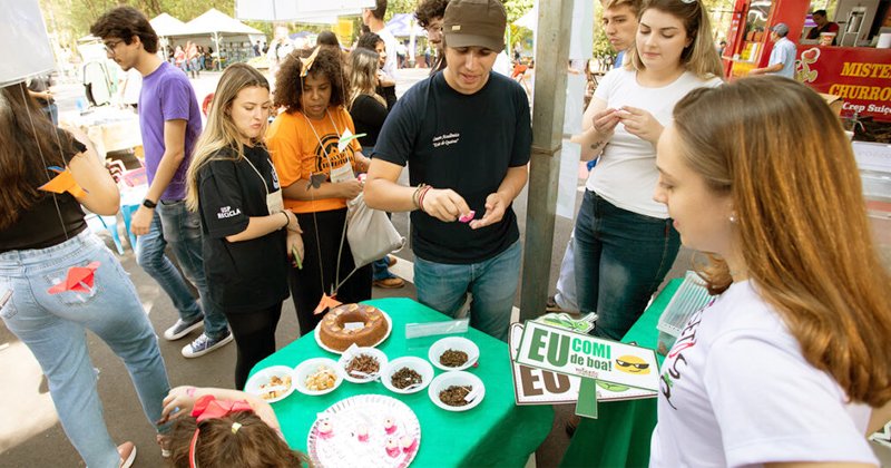 Pessoas numa área ao ar livre em volta de uma mesa com pratos e um bolo