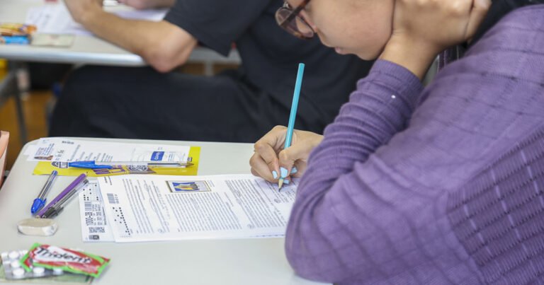 Estudantes sentada numa carteira escolar respondendo as questões de uma prova impressa em papel