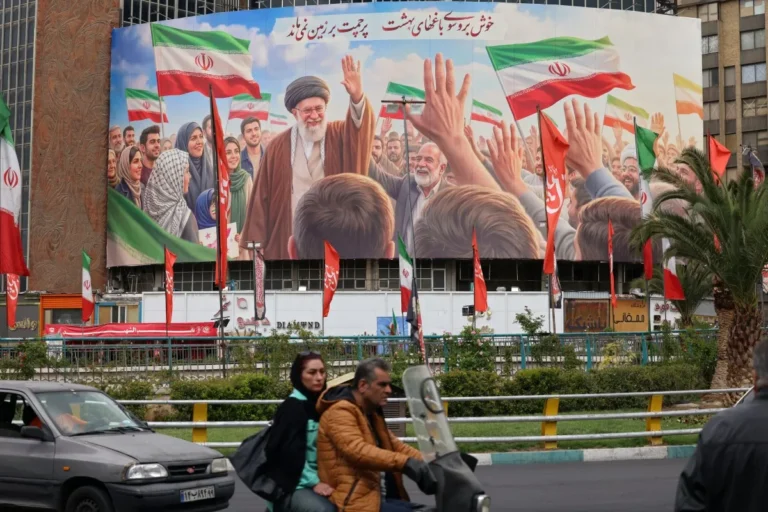 No primeiro plano, um homem pilota uma moto e tem uma mulher como carona. Ao fundo, um grande painel em homenagem à revolução iraniana com bandeiras e líderes religiosos em destaque