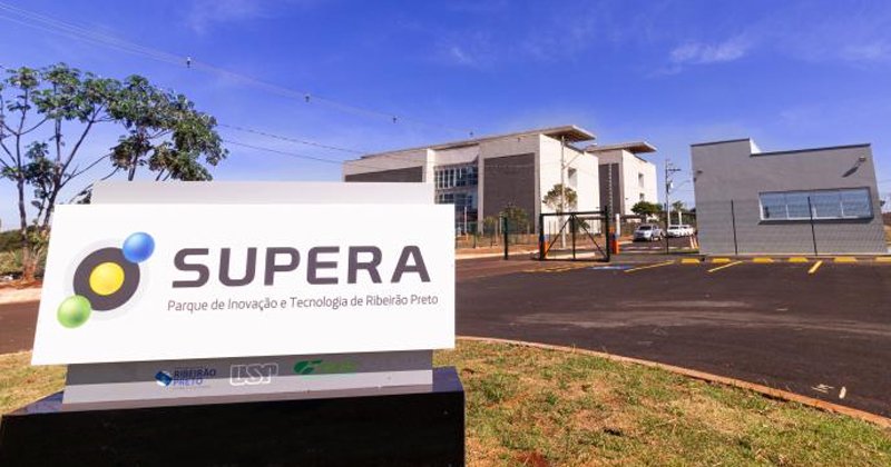 Placa com o nome do Supera Parque e ao fundo alguns prédios que fazem parte do parque de ciência
