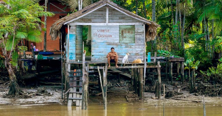 Morador ribeirinho sentado na parte de fora de uma palafita à margem do rio