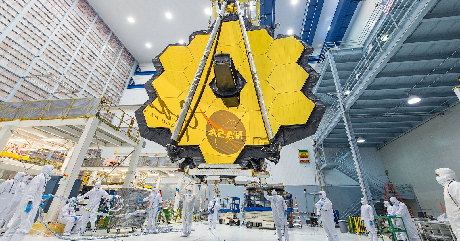 Imagem de uma grande estrutura amarela em com vários losangos e abaixo alguns homens com macacão branco