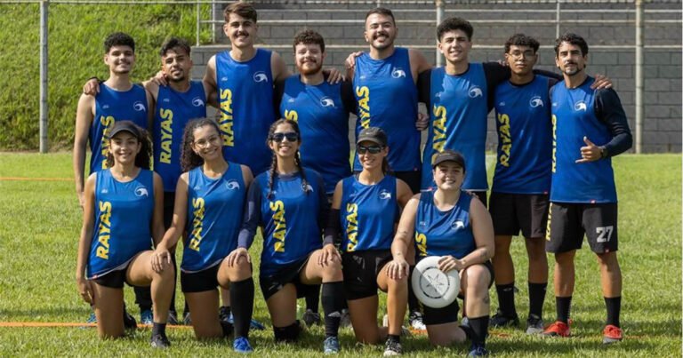 Equipe de Ultimate Frisbee posando em campo gramado, com uniformes azuis e um disco esportivo em destaque.