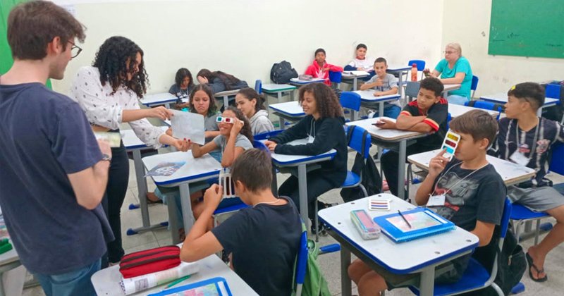 Adolescentes sentados em carteiras numa sala de aula mexendo em materiais