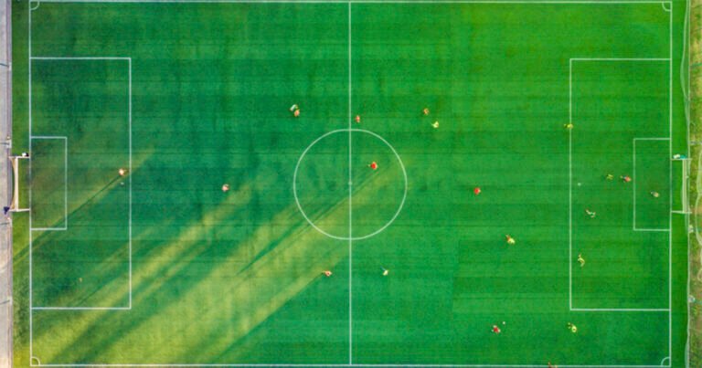 Foto aérea de quadra gramada verde, com jogadores em campo