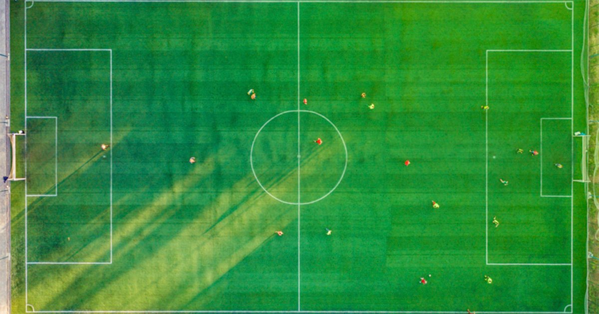 Foto aérea de quadra gramada verde, com jogadores em campo