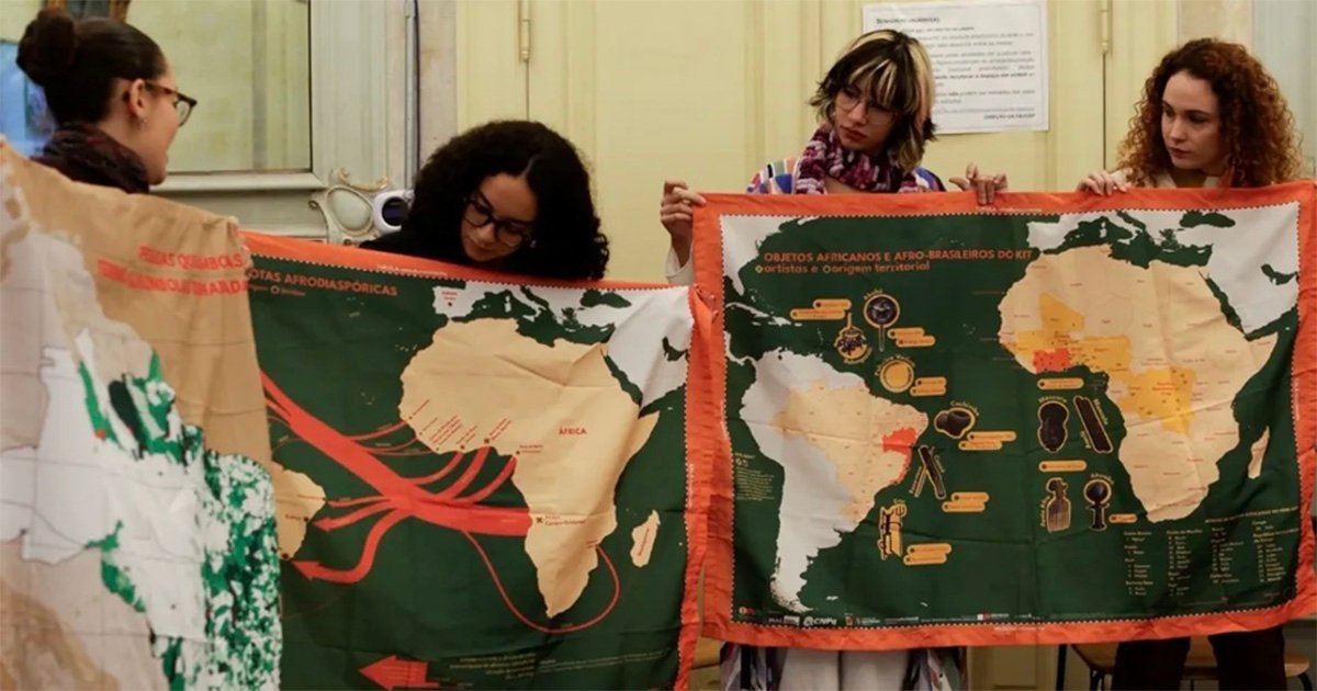 Quatro mulheres seguram pôsteres com mapas ilustrativos da América do Sul e da África